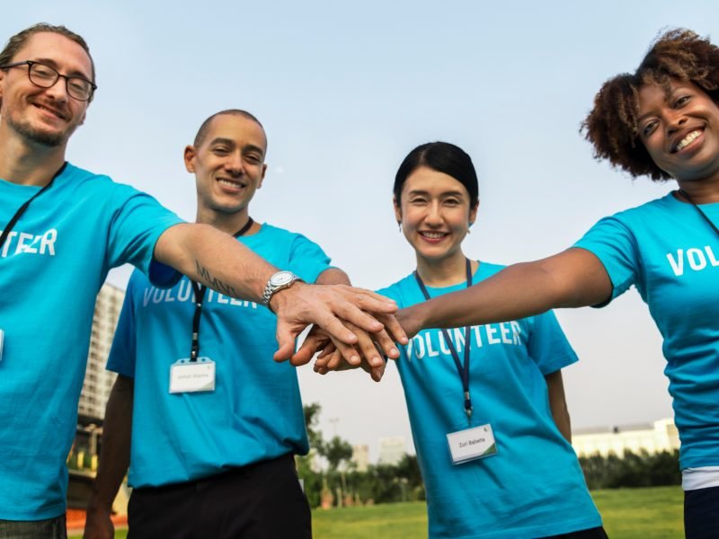 Four volunteers of varying ethnicities touch hands in a team huddle.