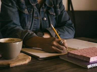 A person writing in a notebook with a pencil.