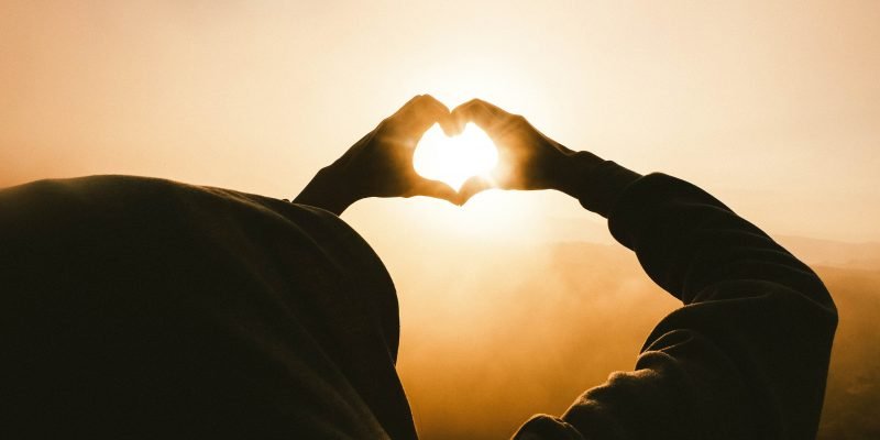 Hands forming a heart looking to the sun.