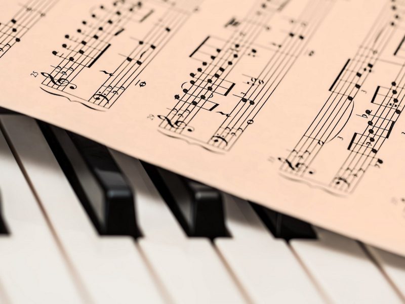 Photo of piano keys with music notes lying on top