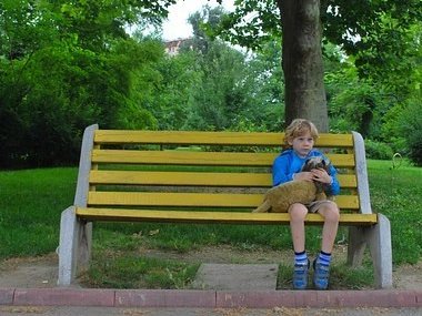 Photo of young boy sitting on a park bench by himself.