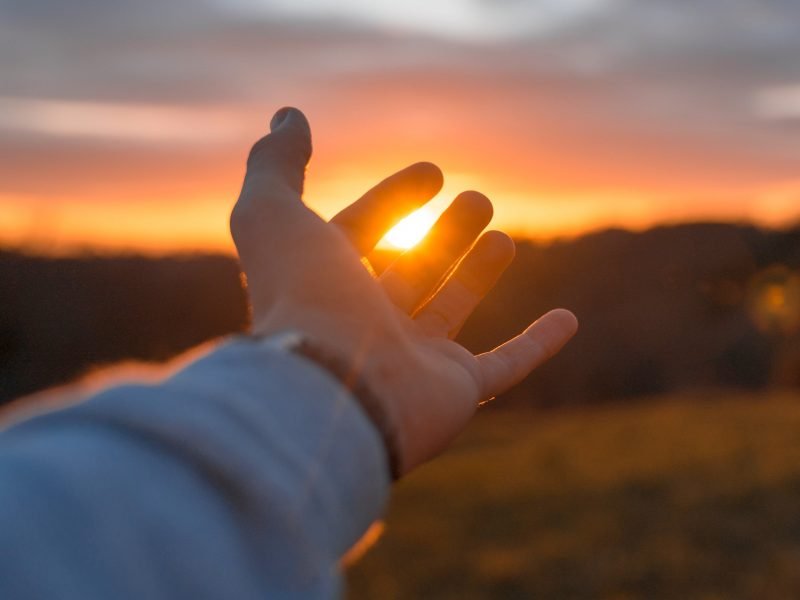 Photo of a hand reaching out toward the sunset.