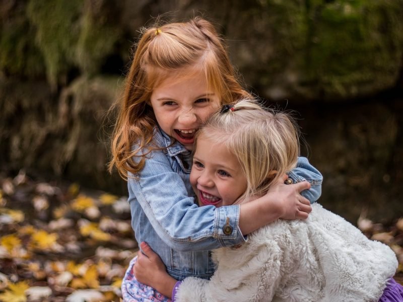 Two small girls hugging each other, not holding back.