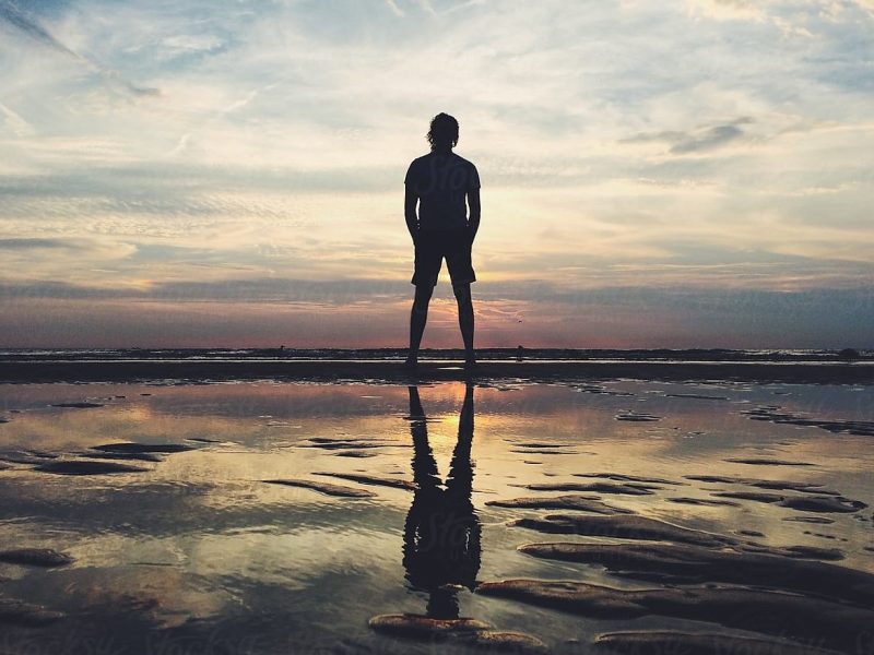 Photo of a person standing on land looking out into the distance of the ocean.