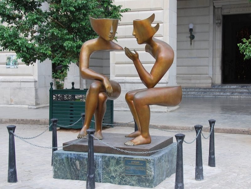 Photo of sculpture showing two people seated speaking with one another.