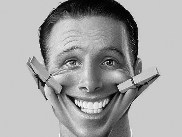Image of a man with a fake smile pinned on with clothes pins at each side of his mouth.