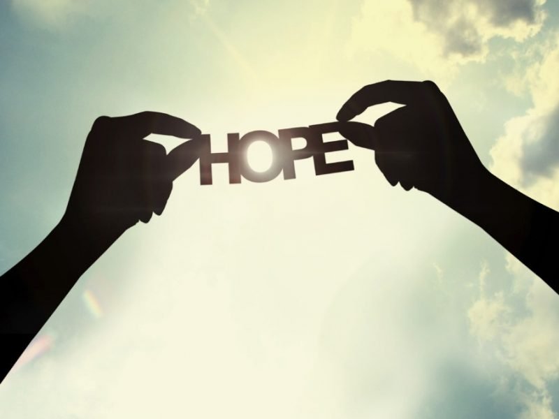 Photo of hands holding a paper cutout of the word Hope.